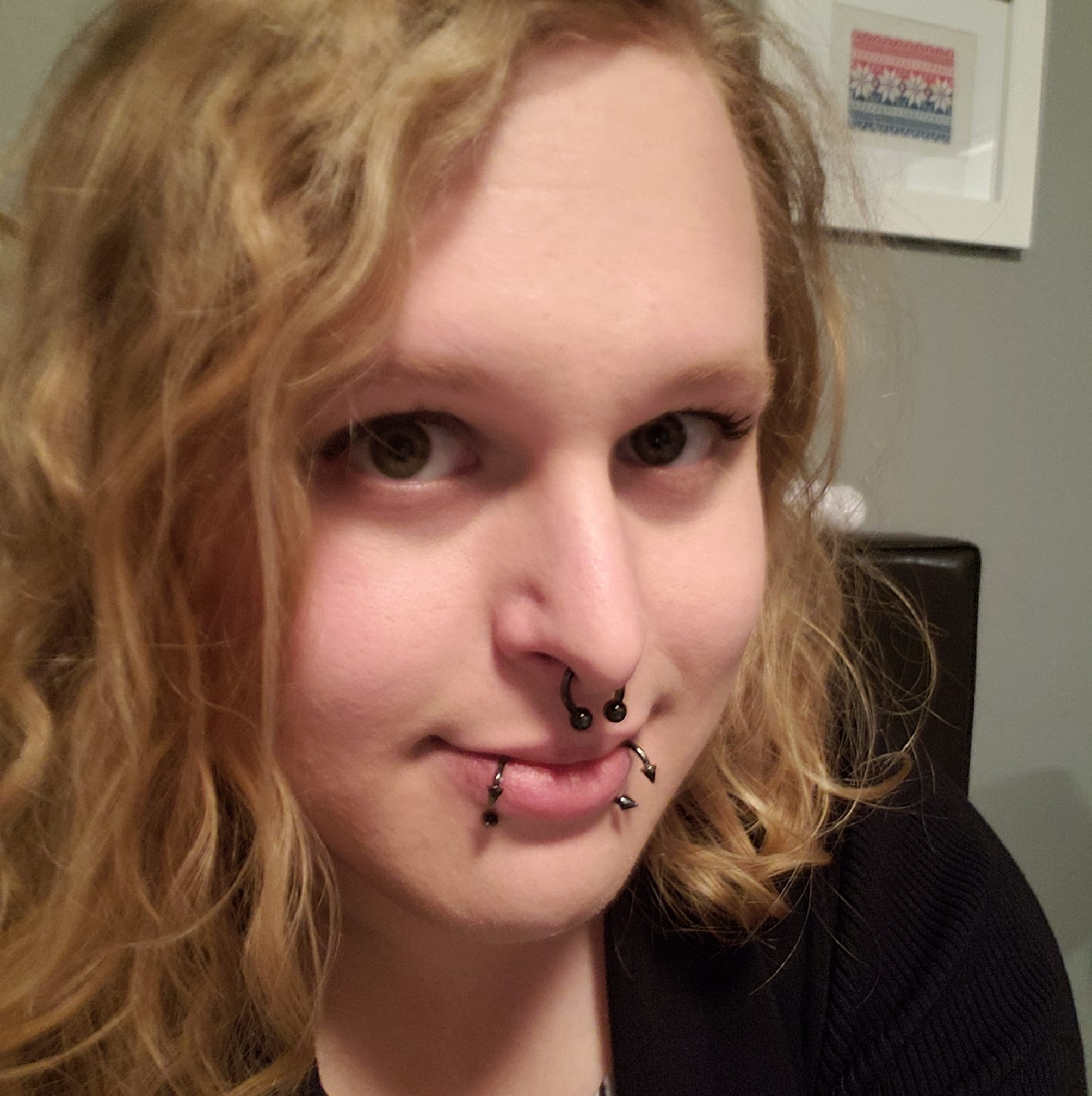 Portrait of Jacq Brasseur, a non-binary white person with long blonde hair and dark rimmed glasses. They are looking out of frame, to the left, with a small smile on their lips.